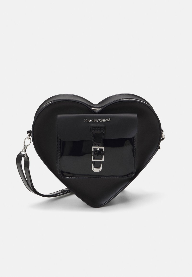 Sac à main noir en forme de cœur avec poche avant à boucle, fermeture éclair argentée et bracelet détachable sur fond blanc.