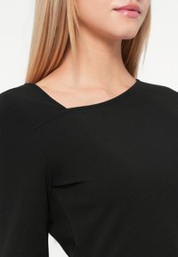 Čierny top s okrúhlym výstrihom, hladkou textúrou a priliehavým strihom. Obsahuje jemné švy na pleciach pre pridanie štýlu.