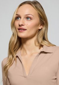 Ljust beige kortärmad polo-shirt med en djup V-ringning, prydd med ett präglat "POLO CLUB"-logotyp på bröstet och en slät yta.