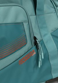 Bolso de lona teal con superficie texturizada, rayas de acento naranja, doble cremallera con tiradores de plástico y un logo de "American Tourister".