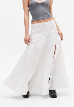 Jupe maxi blanche à plusieurs niveaux, fabriquée en tissu léger avec des détails en dentelle, dotée d'une taille à cordon de serrage et d fentes latérales pour faciliter les mouvements.