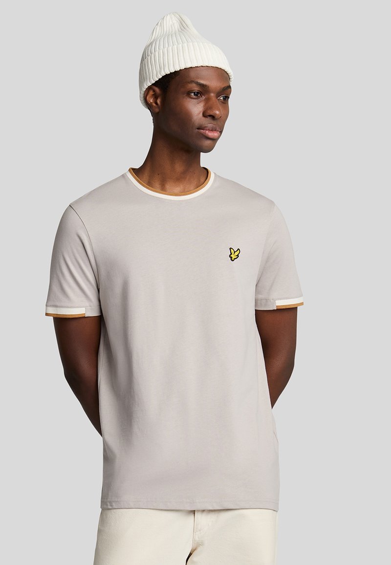 T-shirt grigio chiaro a maniche corte con bordo giallo sul collo e sulle maniche, caratterizzato da un piccolo emblema giallo sul lato sinistro del petto.