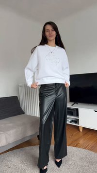 Biela mikina s trblietavým dizajnom na prednej strane, doplnená širokými čiernymi koženými nohavicami a čiernymi lodičkami so špičatou špičkou.