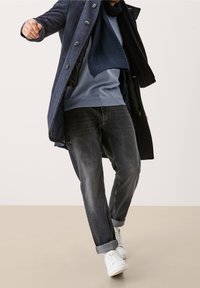 Cappotto blu scuro con bottoni, maglione azzurro chiaro, jeans grigi e sneaker bianche. Il cappotto ha una finitura testurizzata e un design a strati.