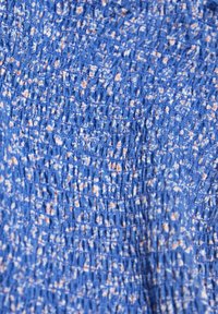 Tissu bleu texturé avec un motif smocké, présentant de petites taches claires uniformément réparties. Matériau durable et extensible avec une apparence froissée.