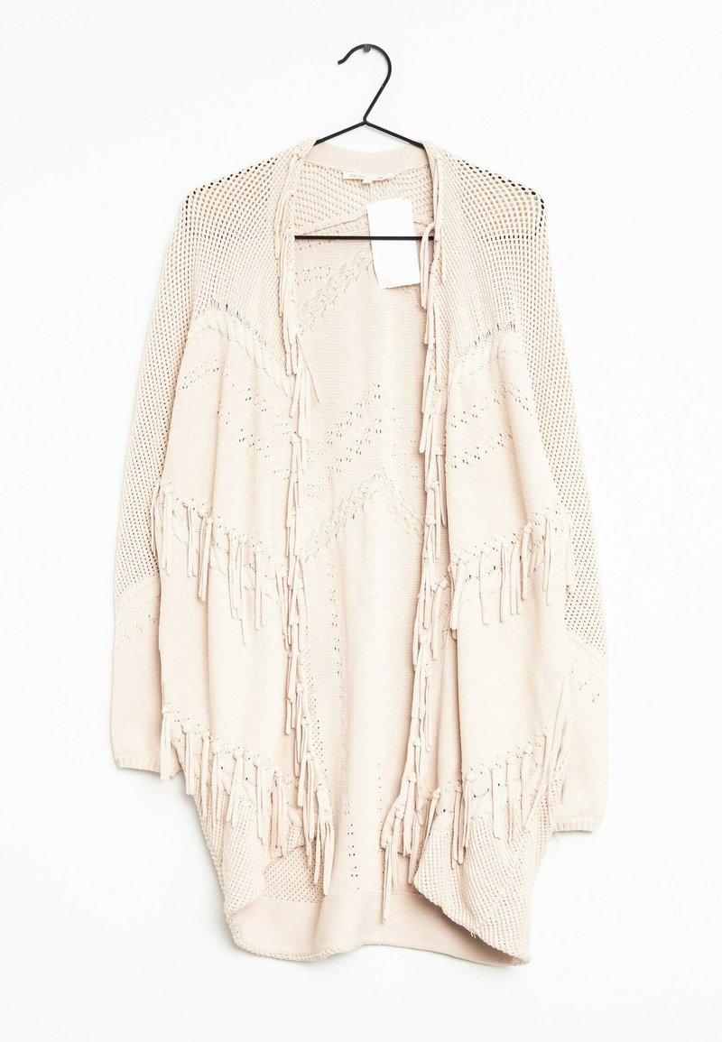 Cardigan beige en tricot avec ouverture sur le devant, motifs texturés et détails à franges, suspendu à un cintre noir sur fond blanc.