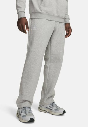 Man draagt lichtgrijze joggingbroek en bijpassende trui met grijze en witte sneakers op een witte achtergrond.