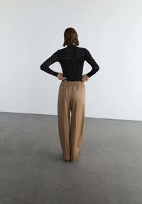 Czarna bluzka z długim rękawem w białe kropki połączona z luźnymi beżowymi spodniami z elastycznym pasem i kieszeniami bocznymi.