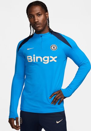 Long-sleeve athletic top in bright blue, featuring a half-zip collar, navy shoulder accents, and a gold logo with text on the front.