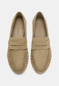 Un paio di mocassini beige in suede con cuciture tipo mocassino e dettaglio a fascia, taglia 37, visti dall'alto su uno sfondo bianco.