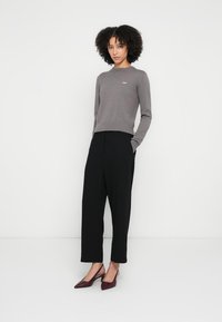 Maglione grigio lavorato a maglia con orlo a coste, abbinato a pantaloni neri dalla vestibilità ampia, indossato con décolleté bordeaux con punta appuntita.