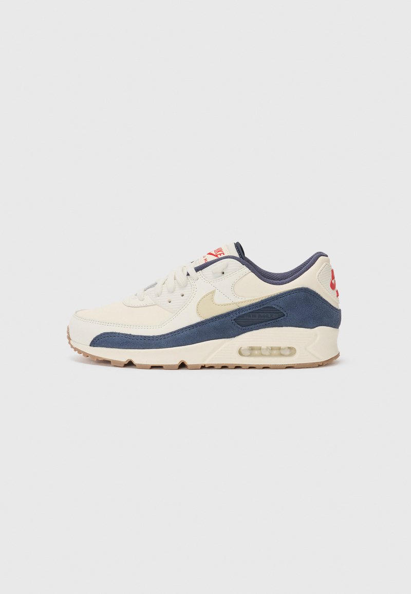 Sneaker mit einem Obermaterial aus cremefarbenem Leder und marineblauem Wildleder, sichtbar luftgefüllter Sohle, beiger Gummisohle und rotem Akzent an der Ferse.