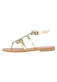 Gold metallic sandal with an open toe design, decorative beaded accents, adjustable ankle strap, and a flat cushioned sole.