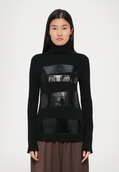 Sort turtleneck sweater med ribbet tekstur. Har blanke sorte rektangulære paneler over brystet og taljen. Lange ærmer, der når til håndleddene.