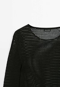 Black knitted sweater with long sleeves and open mesh pattern, round neckline, and a visible label inside the collar.