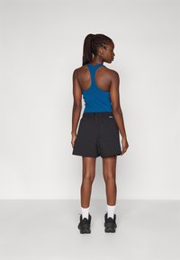 Sorte shorts med to sidelommer, båret sammen med en blå racerback tanktop. Modellen sætter dem sammen med sorte sko og hvide sokker.