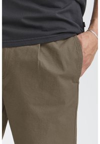 Olive green trousers with a textured fabric featuring a subtle grid pattern. Includes side pockets and a relaxed fit.