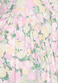 Vestido de tecido floral com cores pastel como rosa, amarelo e verde, com uma textura leve e detalhes franzidos. Acentos de botão visíveis.