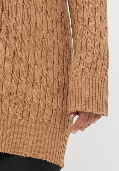 Pull en tricot de couleur beige chaud, avec un design en torche et des poignets côtelés. Le matériau a une texture douce et une coupe décontractée.