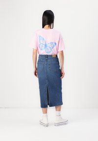 Pink t-shirt with blue butterfly graphic on the back, paired with a high-waisted denim skirt featuring a rear slit and two back pockets.