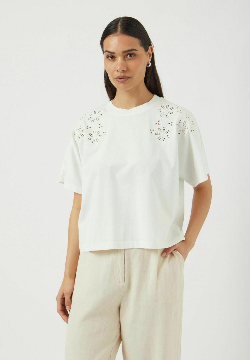 Hvit kortermet skjorte med blomsterbroderi i øyet på skuldrene, laget av et mykt stoff, med rund hals og løs passform.