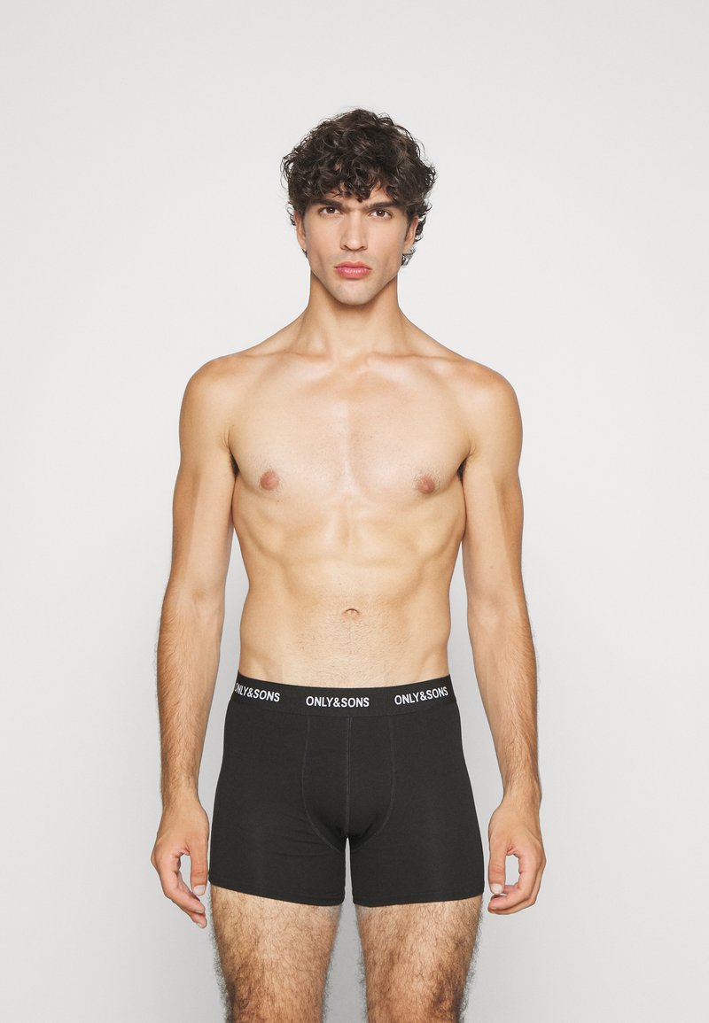 Schwarze Boxer-Shorts mit einem Logo-Bund, eng anliegendem Design, glatter Textur und ohne sichtbare Muster, getragen von einem männlichen Model.
