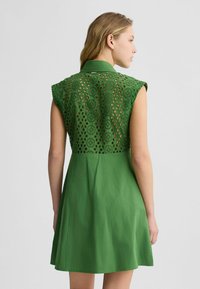 Abito verde con schiena in pizzo trasparente, colletto, maniche a cappuccio e gonna a ruota. Tessuto liscio con motivi dettagliati.