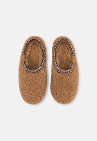 Chaussons en polaire marron avec une texture douce et duveteuse. Bordés d'une couture décorative à l'ouverture. Conception à bout arrondi.