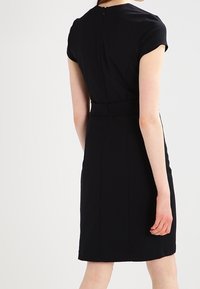 Czarna dopasowana sukienka z krótkimi rękawami, zamkiem z tyłu i wyraźnie zaznaczoną talią. Gładki materiał i długość do kolan. Minimalistyczny design bez wzorów.