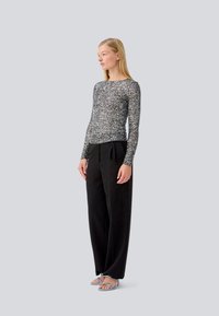 Long-sleeve top in black and silver speckled fabric, paired with high-waisted black trousers and light blue strappy sandals.