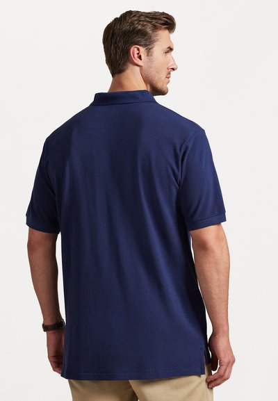 Jūras spēku zila polo krekls ar īsām piedurknēm, apkakli, sānu šķirbām un teksturētu audumu. Izstrādāts ar brīvu piegriezumu un vienkāršu konstrukciju.