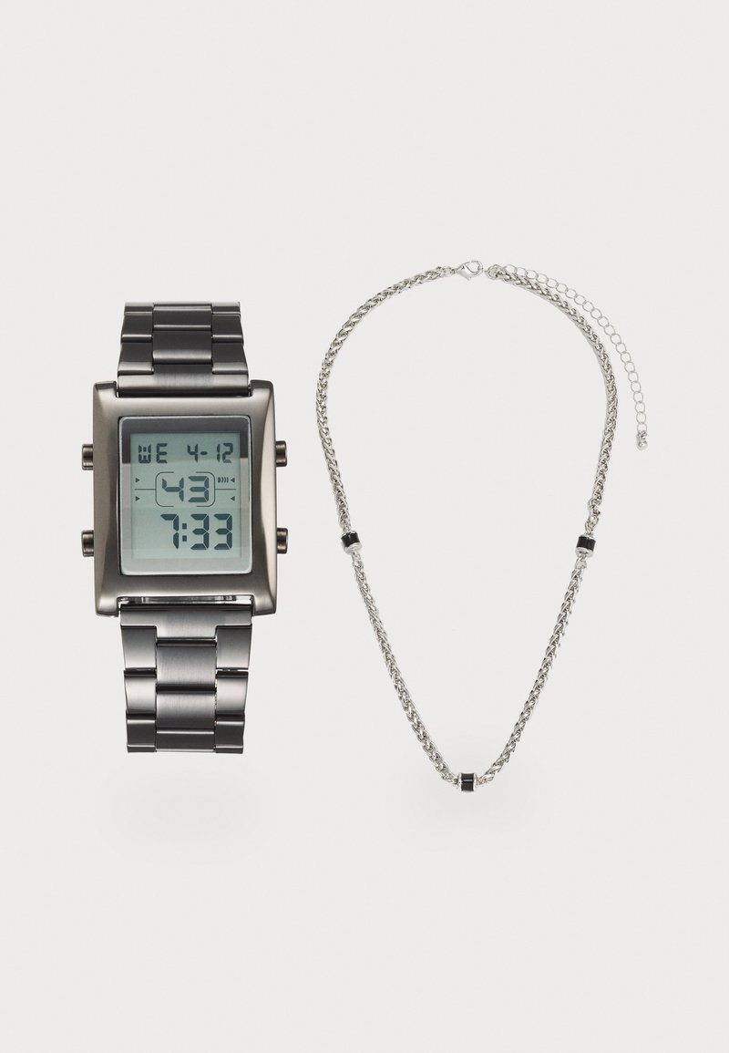 Montre numérique avec un cadran carré, bracelet en métal noir, et un collier en chaîne argenté avec des accents noirs et argentés alternés.