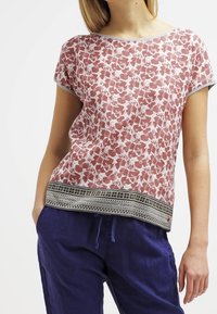 Rood-witte katoenen top met bloemenprint en korte mouwen; voorzien van een geprint zwarte zoom. Gepaard met losse blauwe broek.