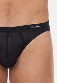 Schwarze Baumwollunterhose mit glatter Textur, niedrig geschnittenem Design und einem dezenten Logo-Tag am Bund. Sie bietet eine enge Passform und minimalen Schutz.