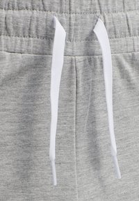 Grå sweatpants med en texturerad tygkvalitet, elastisk midjeband och vit dragsko med plastaglets. Närbild på midjeområdet.