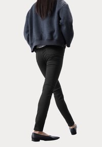 Vaqueros ajustados negros con bolsillos traseros y un talle medio, combinados con un sudadera texturizada gris oscuro y recortada, y zapatos planos negros.