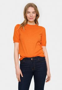 Bluză scurtă portocalie, cu gât rotund și umeri pliați, asociată cu blugi negri din denim, prevăzuți cu un nasture și cinci buzunare.
