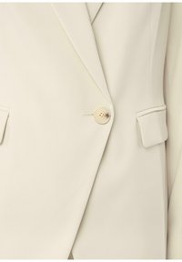 Beżowa marynarka dopasowana, zapinana na jeden guzik, z klapami w kształcie notch, bocznymi kieszeniami i gładką fakturą materiału.