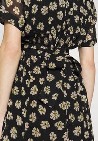 Robe noire avec un motif floral comportant des fleurs roses et vertes, taille élastique et une ceinture nouée à la taille. Manches courtes, tissu léger.