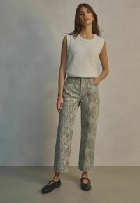Wit mouwloos topje met ribgebreide halslijn, gestreepte grijze slangenprint broek en zwarte platte schoenen. Eenvoudig ontwerp met een rechte pasvorm.