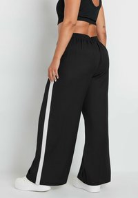 Czarne spodnie typu wide-leg z miękkiego materiału, z białym paskiem po bokach. Elastyczny pasek w talii i luźny krój dla wygody.