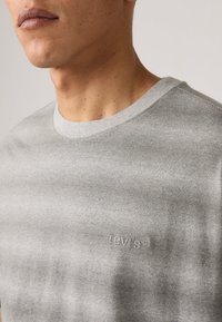 Gråstripet t-skjorte laget av myk stoff, med ribbestrikket halsringning og subtilt brodert logo på brystet.