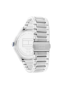 Reloj de acero inoxidable plateado con una correa pulida, caja octagonal y corona azul. La parte trasera muestra el nombre de la marca y los detalles de resistencia al agua.