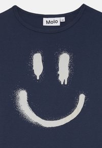 Camiseta de algodón color azul marino con un gran diseño de cara sonriente pintada con spray en blanco, que presenta detalles texturizados y un cuello redondo.