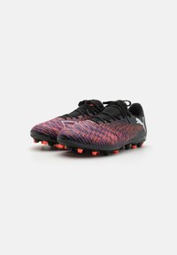Botas de fútbol negras y moradas con una parte superior texturizada, acentos naranjas y suelas negras con tachones; con un diseño de cordones y logo lateral.