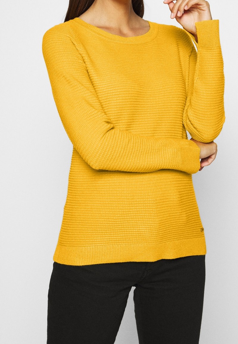 Pull jaune en tricot avec une texture côtelée, col rond et manches longues ; présente une coupe légèrement décontractée et un ourlet droit.