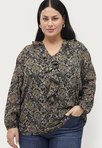 Zwarte blouse met een paisleypatroon in blauw, groen en beige. Heeft een gerimpelde halslijn en lange mouwen. Draagt bij jeans.