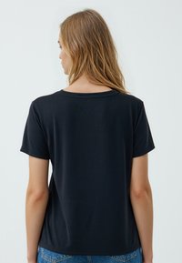 T-shirt nera a maniche corte con colletto rotondo, realizzata in tessuto morbido, con una vestibilità comoda e un design minimalista, vista da dietro.