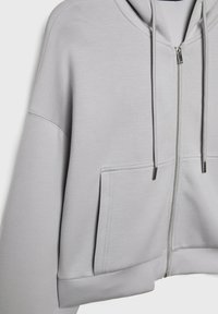 Hellgraue, kurze Kapuzenjacke aus weichem Material, mit einem Reißverschluss vorne, verstellbaren Kordeln und einer Kängurutasche.