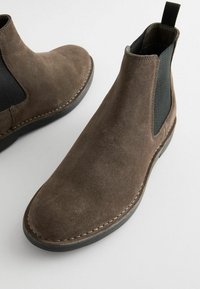 Bottines Chelsea en daim brun avec des panneaux élastiques sur les côtés, bout arrondi et détail de couture contrasté le long de la semelle. Texture lisse et design élégant.